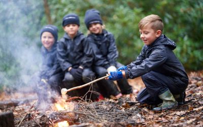 Primary kids roasting marshmallows in the woods smiling